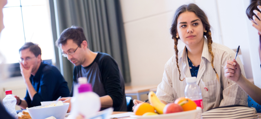 A group sat around a table, mid meeting, pens in hand ready to collaborate with each other.